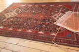 Antique Qashqai rug corner showcasing wine red main border and complex floral patterns.