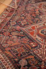 Antique Qashqai rug's intricate field, dense with tribal plants, vinery, madder red, and navy.