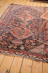 Antique Qashqai rug corner: dense geometric, stylized motifs, madder red and navy, aged fringe.