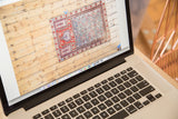 Geometric antique Caucasian prayer fragment rug with red and blue tones on laptop screen.
