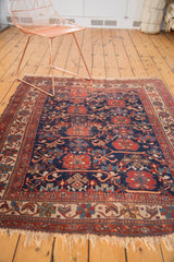 Antique Afshar rug corner with patterned border in cherry red, cream, and navy, highlighting tattered fringe.