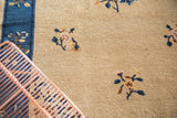 Delicate stylized floral vinery on a beige antique Peking carpet field and blue border.