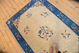 Art deco stylized Peking carpet with open beige field, delicate blossoms, and indigo blue border.