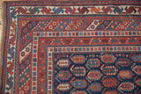 Intricate geometric borders and navy, red boteh motifs on an antique Afshar rug corner.