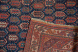 Folded corner of an antique Afshar rug, showing natural fringe and geometric border reverse.