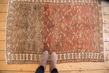 Distressed Northwest Persian rug, overhead with feet, highlighting dramatic abrash and earthy tones.