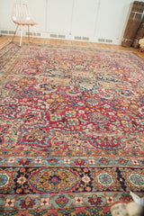 Layered borders of the antique Kerman, featuring navy, cochineal red, and dusty gold floral motifs.