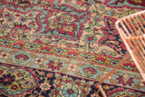 Curvilinear mil fleur pattern detail on an antique Persian Kerman rug with cherry, navy, and aged gold tones.