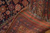 Antique Kamseh rug corner, showing light tatter, fringe, and striped flat-woven back.