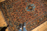 Antique Qashqai rug corner with worn fringe, navy border, and Herati-inspired madder field.