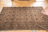 Distressed vintage Afghan rug corner, showcasing worn gul motifs and intricate chocolate borders.