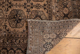 Lifted corner of vintage distressed Afghan rug reveals woven back and faded gul motif.