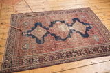 Distressed Senneh rug showing a navy blue medallion cartouche, cherry red herati field, and visible wear.