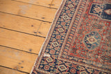 Distressed Senneh rug corner with fringe, indigo geometric border, and cherry red herati motif.
