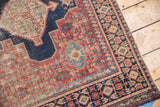 Distressed vintage Senneh rug corner, highlighting intricate navy blue, cherry red, and ivory border motifs.