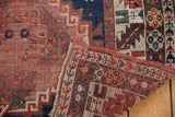 Detail of antique Kazak rug showing hand-knotted foundation, geometric patterns, and worn red and navy pile.