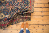 Folded section of an antique Caucasian Soumac carpet, revealing navy, red, and ivory tribal motifs.