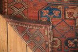 Vintage Afghan rug corner, madder red pile, blue gul patterns, brown side, raw fringe.