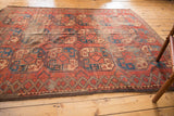 Vintage Afghan carpet's geometric diamond border, red gul pattern, and areas of exposed foundation.
