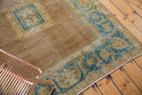 Distressed Agra rug corner, sky blue and dusty gold serrated leaf border on pale brown field.