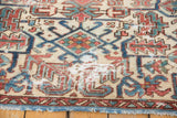 Distressed Heriz fragment carpet: geometric ivory, blue, red patterns, visible wear, blue fringe.