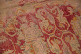 Oushak carpet texture showing oversized patterns in raspberry red, pale gold, and silver.