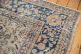 Distressed vintage Sparta carpet corner, with worn fringing and faded blue floral motifs.