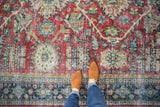 Distressed vintage Mahal carpet detail: worn ruby red field meets a rich navy teal border.
