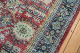 Corner view of distressed vintage Mahal carpet, showing worn ruby red field and navy border.