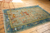 Distressed corner of an antique Peking rug, with sky blue cloudband border and worn pictorial field.