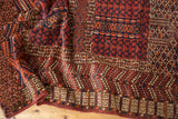 Geometric serrated leaf and rams horn patterns in terracotta, navy, and ivory on a vintage rug.