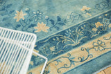 Distressed texture and faded floral vine motifs in sky blue and ivory on an antique Peking rug.