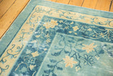 Distressed floral vine border in sky blue and pale gold on an antique Peking carpet.