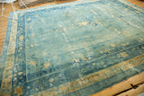 Visible distressing of sky blue and pale gold floral patterns on an antique Chinese rug.