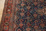 Vintage Qashqai carpet corner with low pile, navy blue field, and madder red zigzag border.