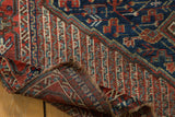 Folded vintage Qashqai carpet corner, revealing hand-knotted weave and patterned pile.