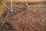 Vintage Qashqai carpet showing dusty rust field, navy geometric rams horn motifs, and tattered edge.