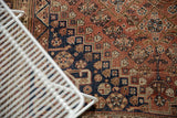 Detail of vintage Qashqai carpet showing terracotta, navy, and ivory geometric floral motifs with even pile wear.