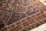 Intricate chestnut, navy, and ivory geometric borders on the antique Kamseh rug, with light fringe tatter.