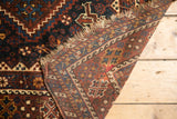 Antique Kamseh carpet corner shows hand-knotted weave, tribal red and blue patterns, and tattered fringe.