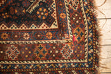 Antique Kamseh carpet corner: geometric floral motifs in navy, chestnut, and tattered edge.
