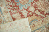 Distressed Tabriz rug corner reveals faded cherry red pile and light hand-knotted foundation.