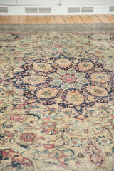 Antique Kermanshah carpet's intricate navy medallion and ivory field with detailed floral motifs.