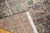Worn floral patterns, visible woven foundation, and a pink edge tape on an antique Kermanshah rug corner.