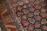 Vintage Heriz carpet showing geometric boteh pattern, navy ground, brick red, and visible pile wear.