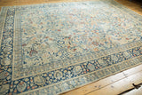 Corner of a vintage Tabriz carpet, showing faded navy border and ivory field with scrolling palmettes.