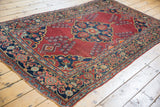 Vintage rug showing cherry red field with vase floral motif, dusty navy border, and light low pile.