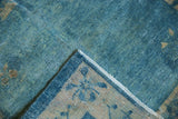 Distressed vintage Peking rug corner showing low blue pile, exposed knot heads, and floral border.