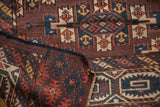 Folded corner of antique Turkmen carpet, revealing plum field, geometric guls, and fringed edge.