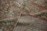 Folded corner of distressed Mahal rug showing worn copper henna plant motif and foundation.